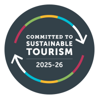 Circular badge with colored arrows, reads: Committed to Sustainable Tourism 2025-26.