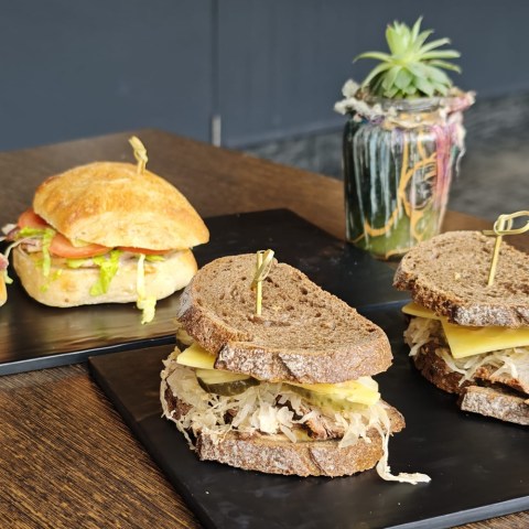 Two rye sandwiches and one ciabatta sandwich on black plates with a jar plant in the background.