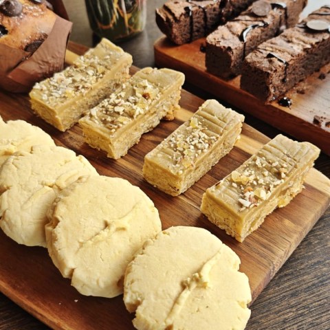 Assorted cookies and pastries on a wooden board, including round cookies and nut-topped slices.