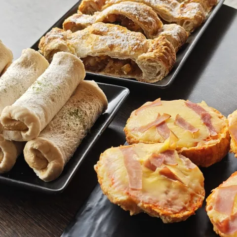 Pastries and bread rolls on black plates, including croissants and toast with cheese and ham.